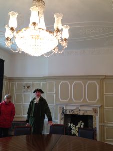 Gentleman in tricorn hat and green coat, in spacious, cream panelled room