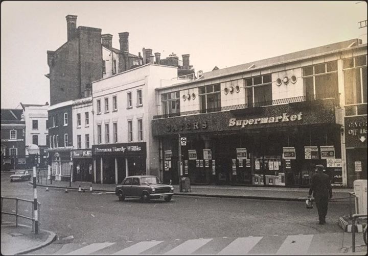 Early supermarket with price posters and portholes between upper floor windows