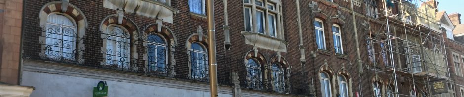 ornate turn of the century building with juliette balconies and buddliah growing out of it