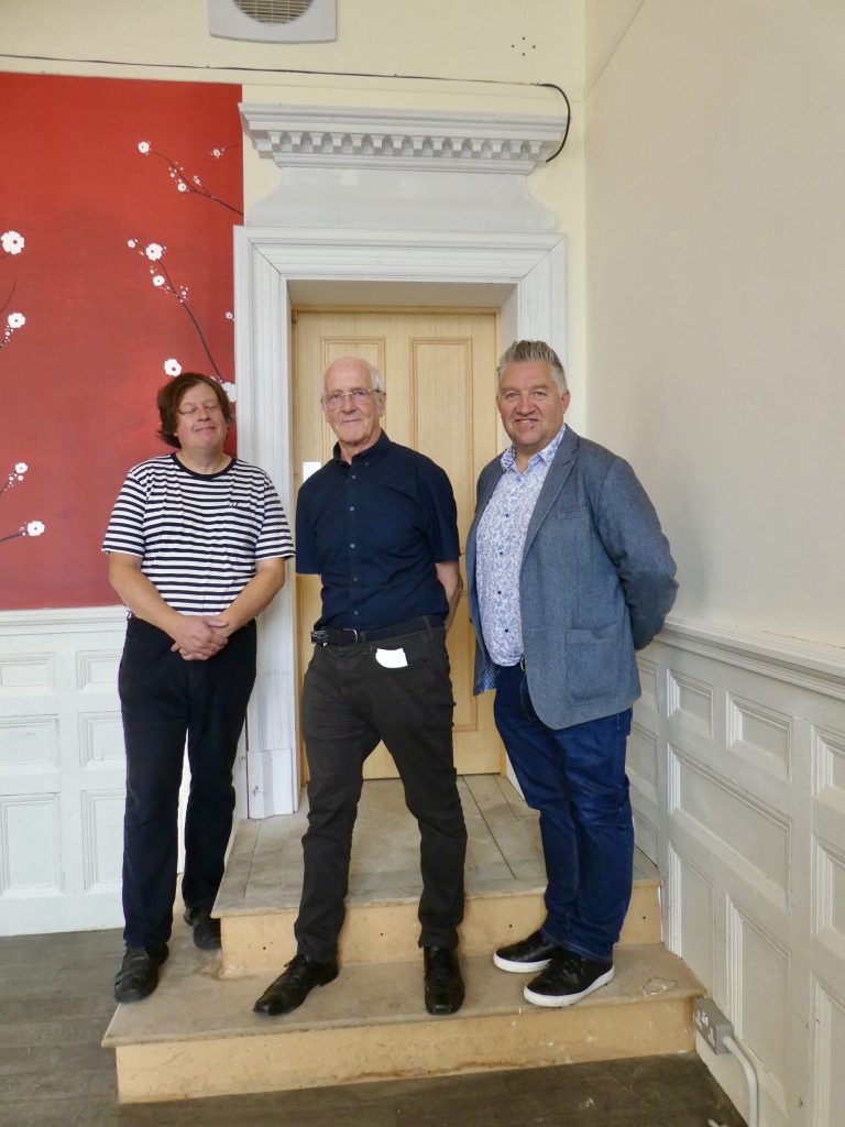 three chaps standing on the steps of a door